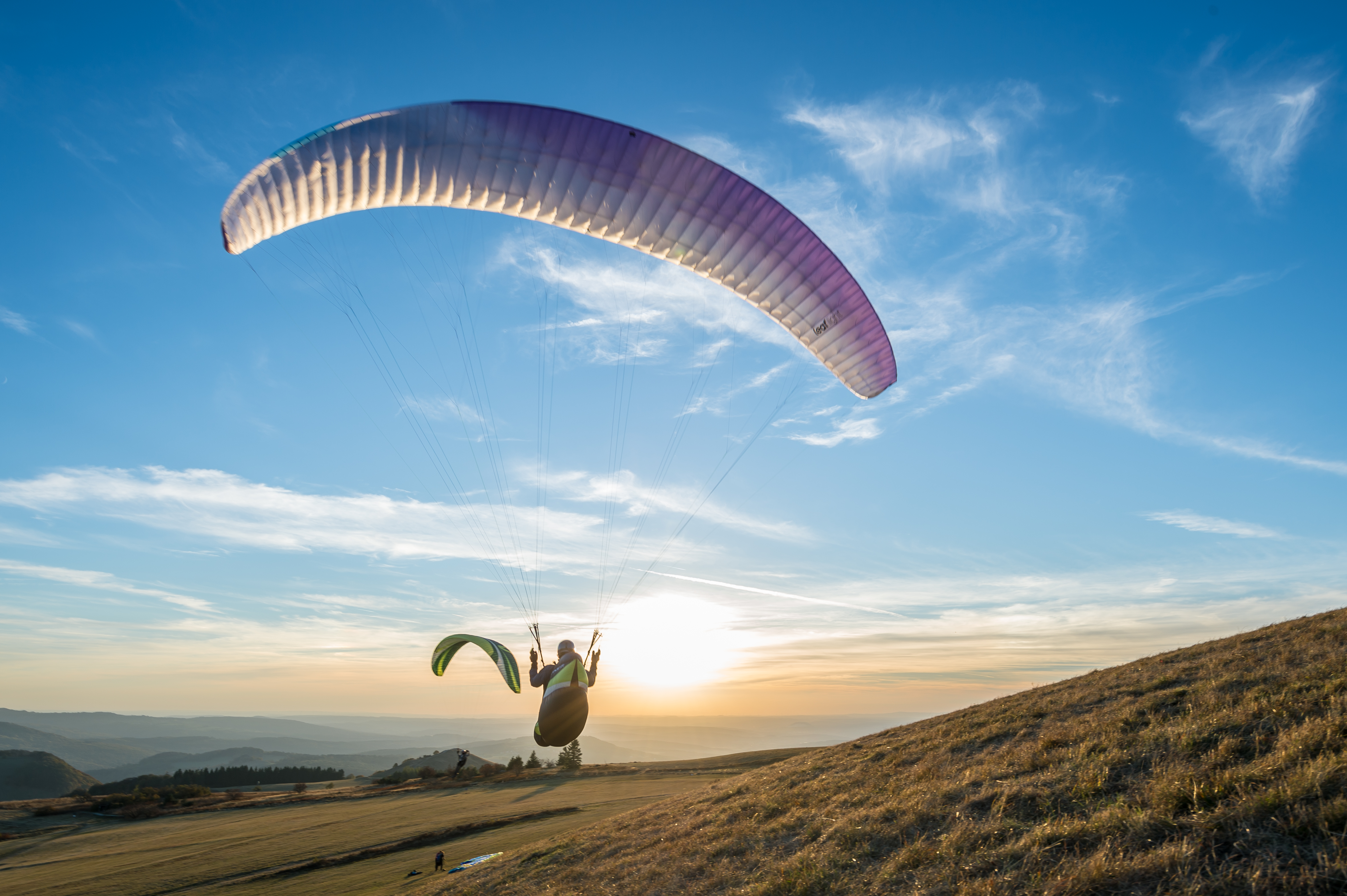 Gleitschirmflieger in der Luft mit Sonnen im Hintergrund.