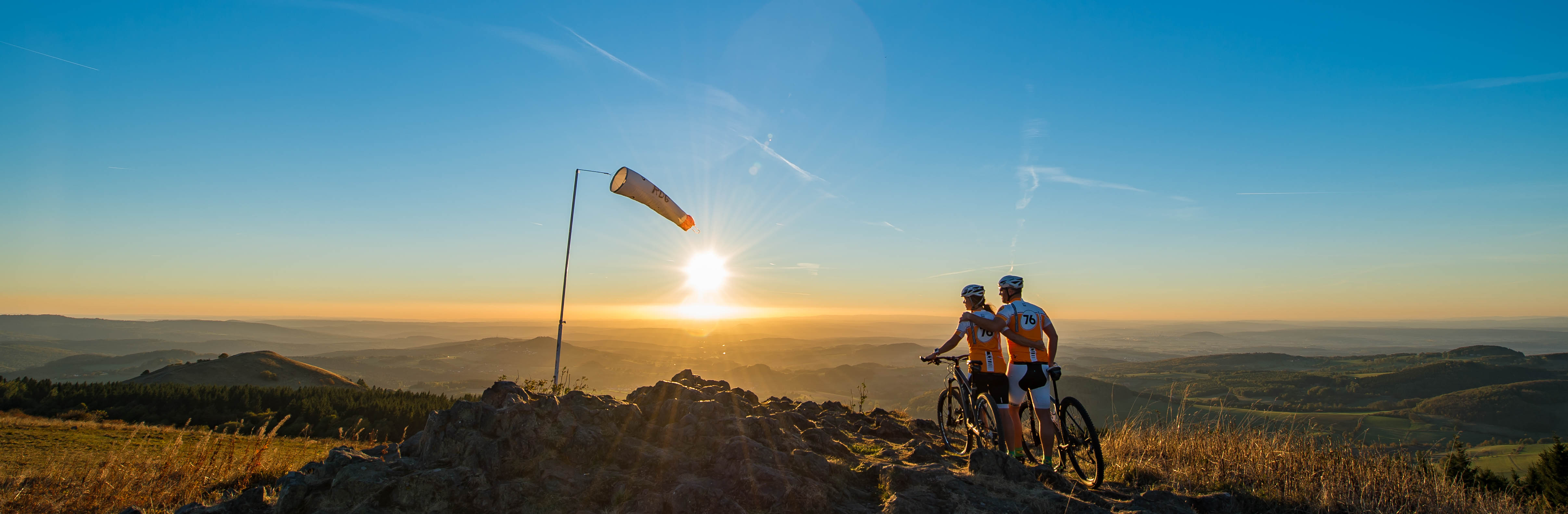 Zwei Mountainbike Fahrer stehen auf einem Gipfel mit den Fahrrädern und blicken in die Rhöner Landschaft.