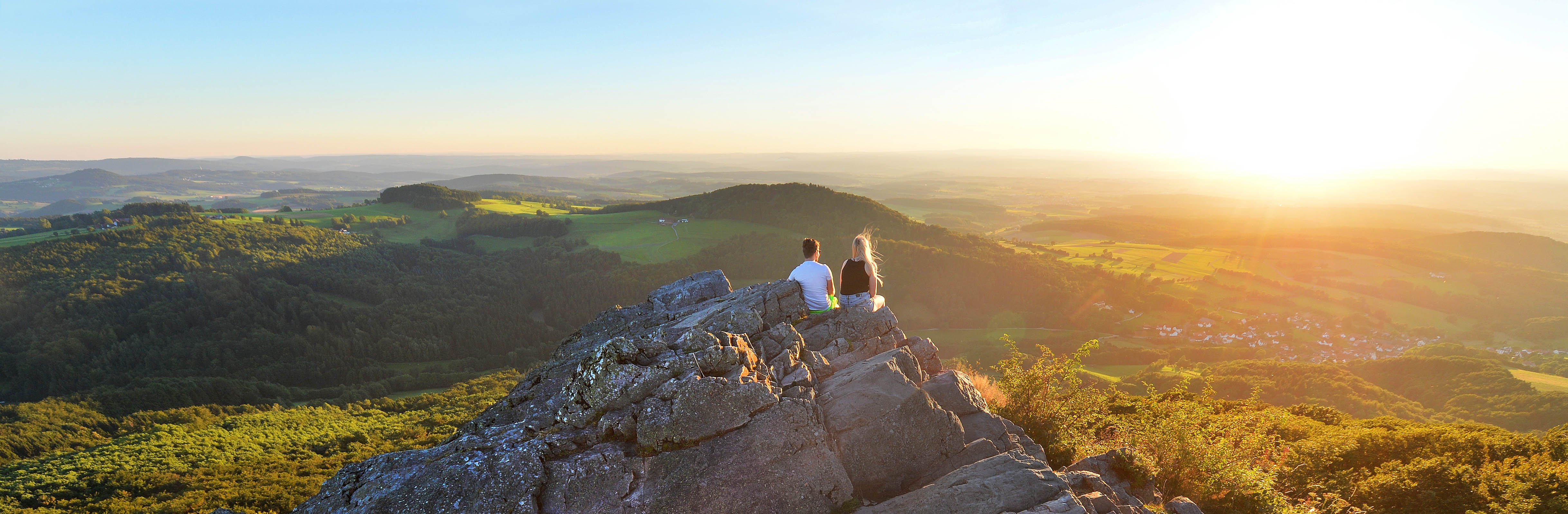 Zwei Personen sitzen auf einem Felsen und Blicken in die Rhön.