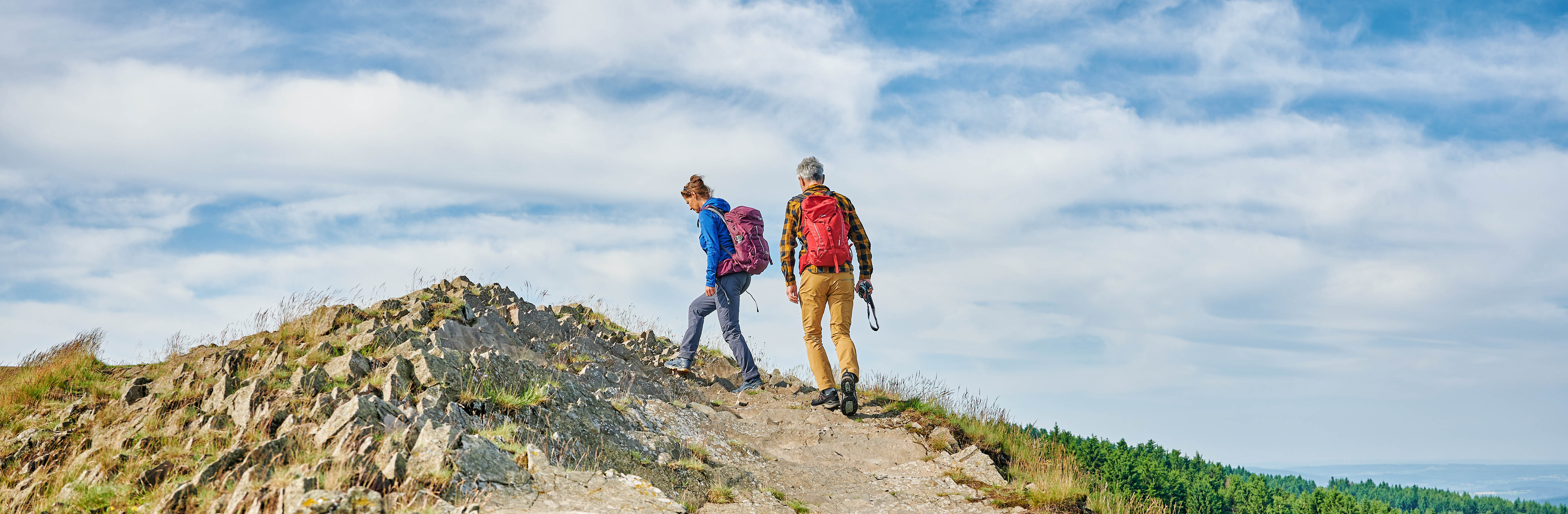 Mann und Frau laufen durch felsige Landschaft.