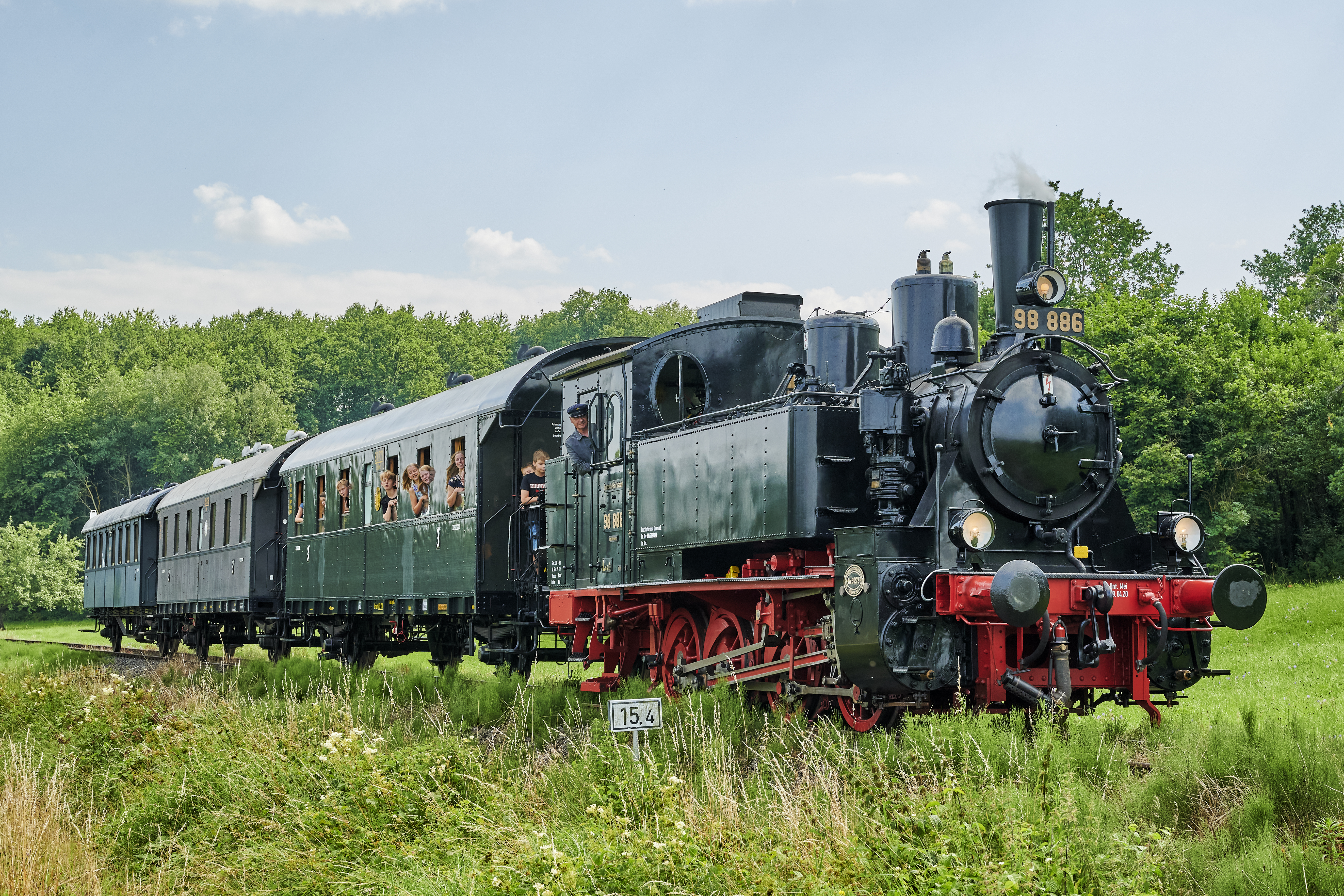 Alte Dampflok mit Personen, die aus dem Wagon herausschauen.