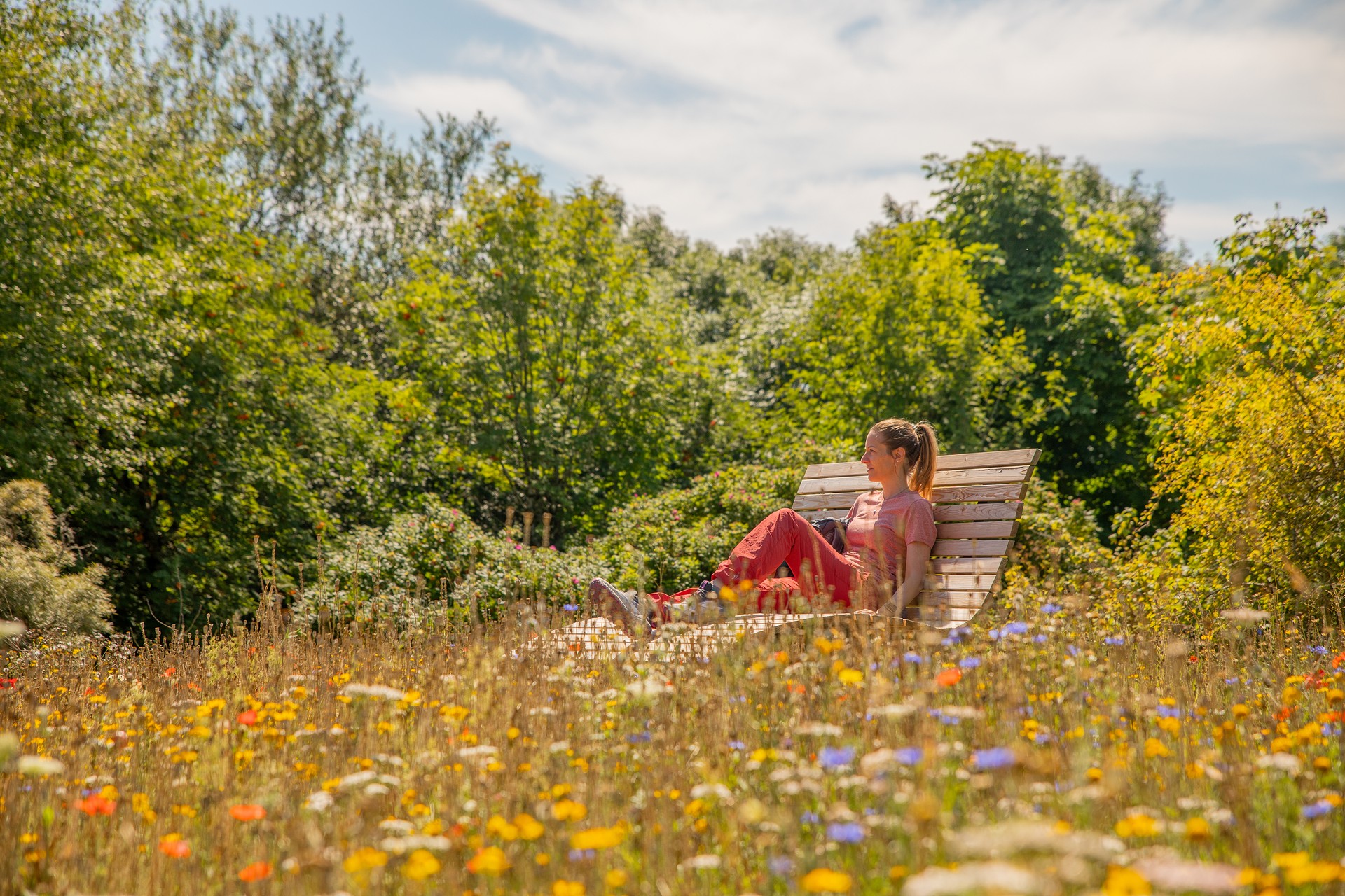 Eine Wanderin sitzt auf einer Bank zwischen bunten Blumen.