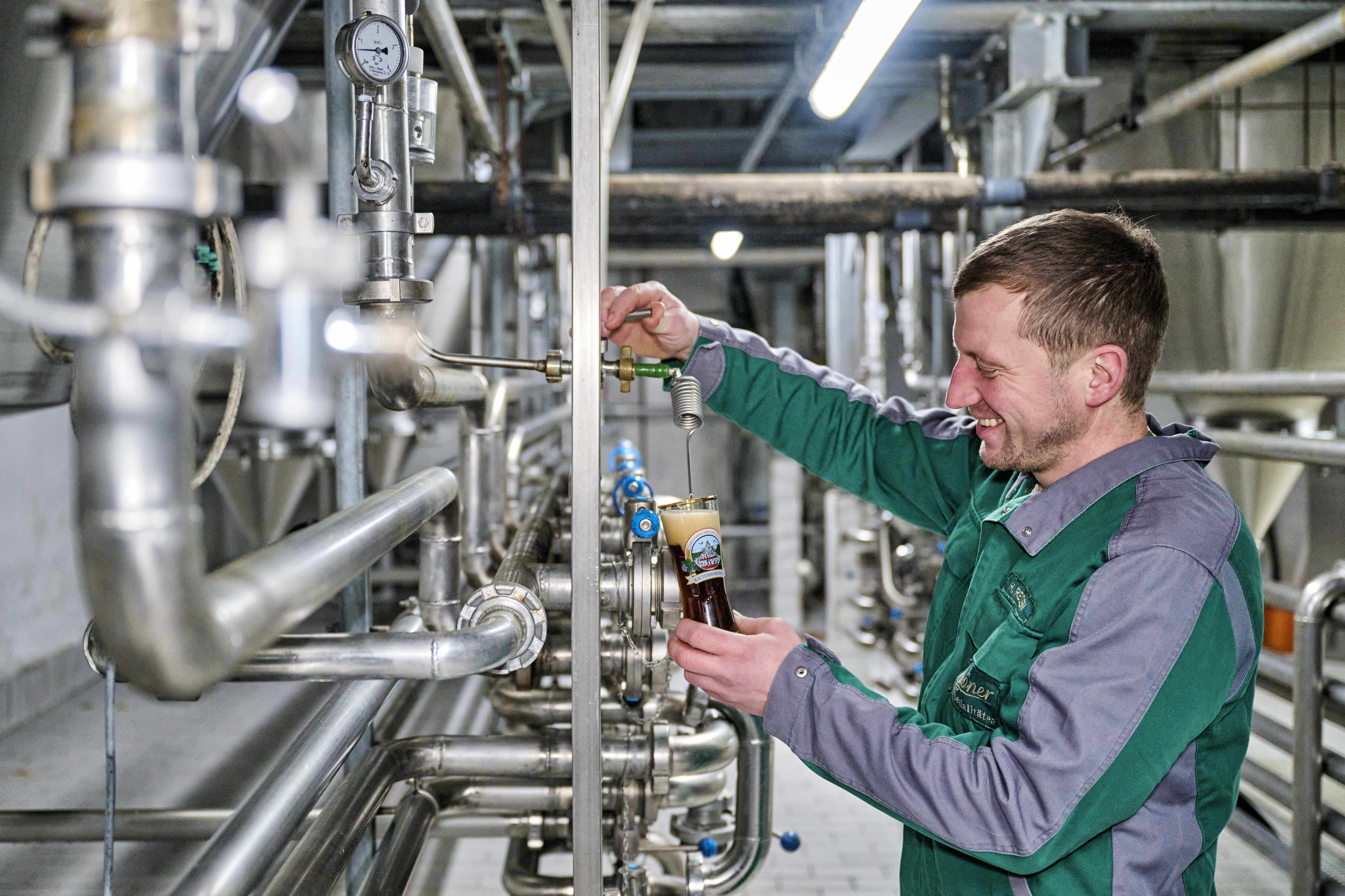 Brauer hält ein kleines Bierglas und zapt aus einer Anlage Bier ab.