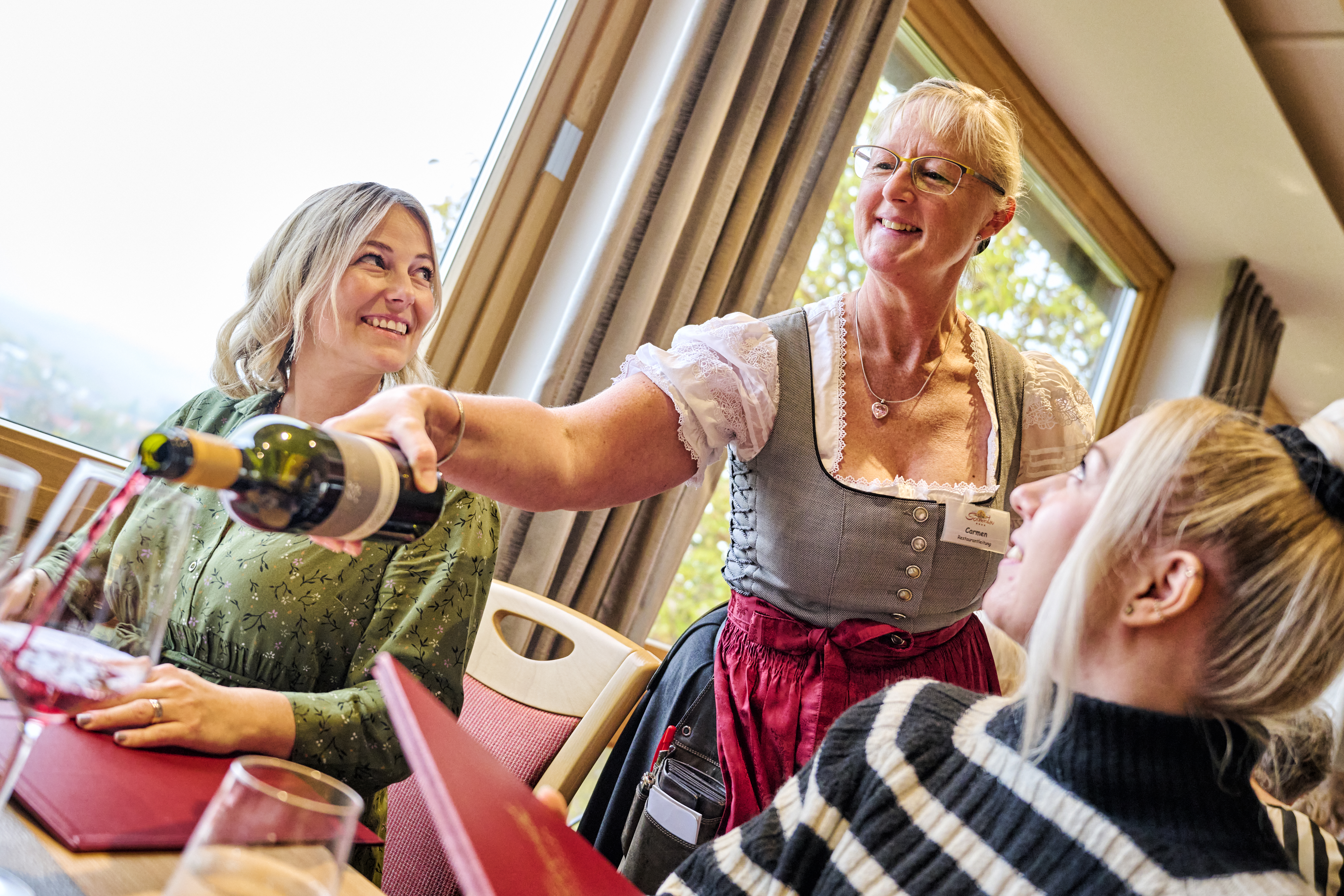 Gastwirtin schenkt Gästepaar Wein ein.