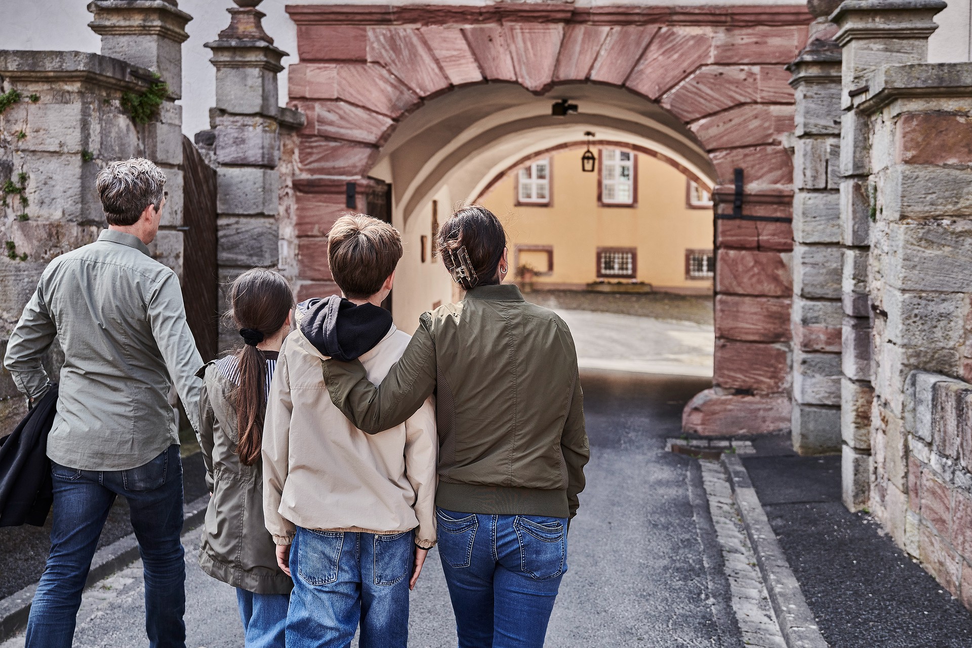 Mutter, Vater und zwei Kinder laufen durch eine Stadt, die einen steinernen Torbogen hat.
