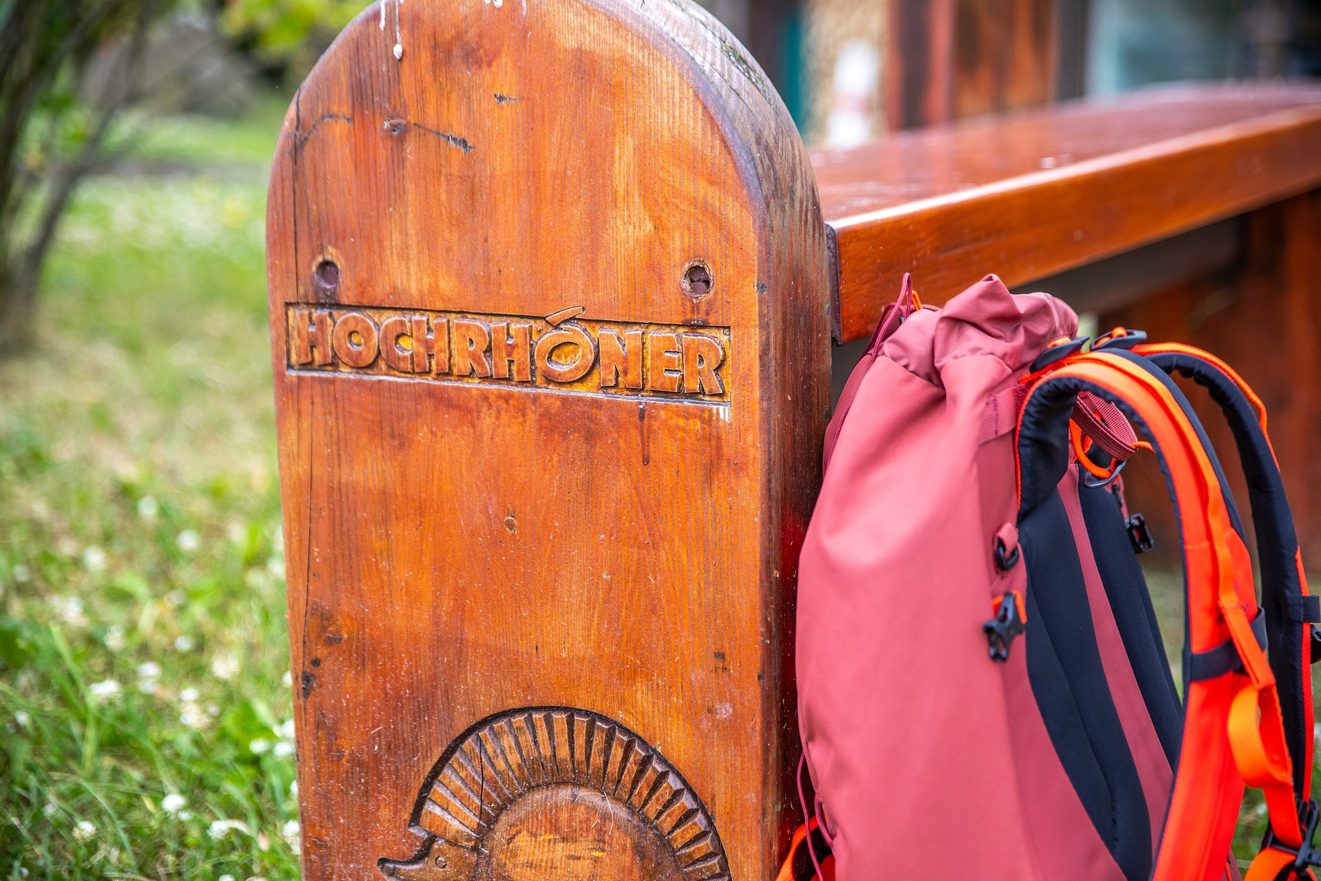Holzbank mit Aufschrift "HOCHRHÖNER". Daran lehnt ein roter Rucksack.