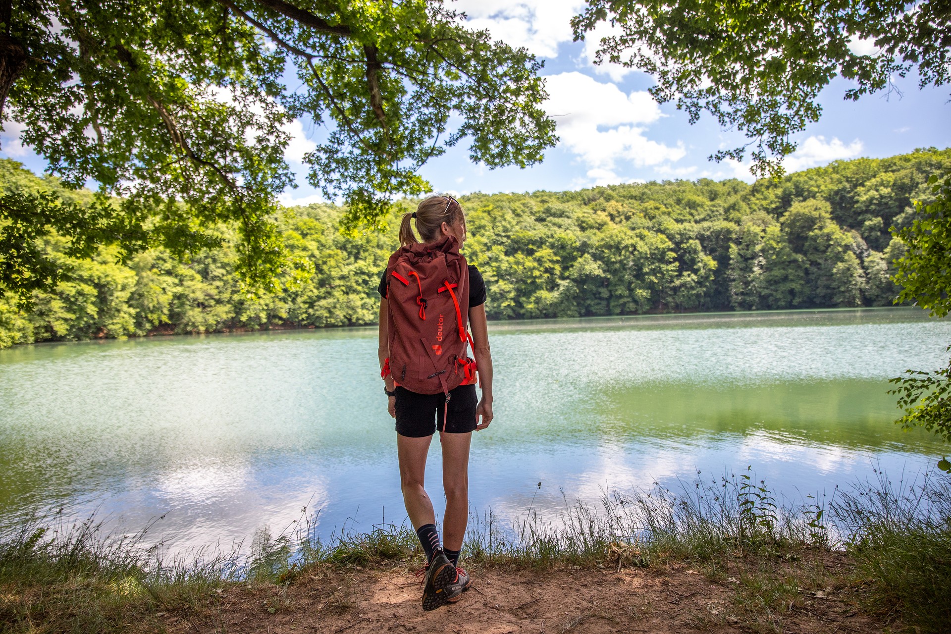 Wanderin steht mit dem Rücken zur Kamera am See.