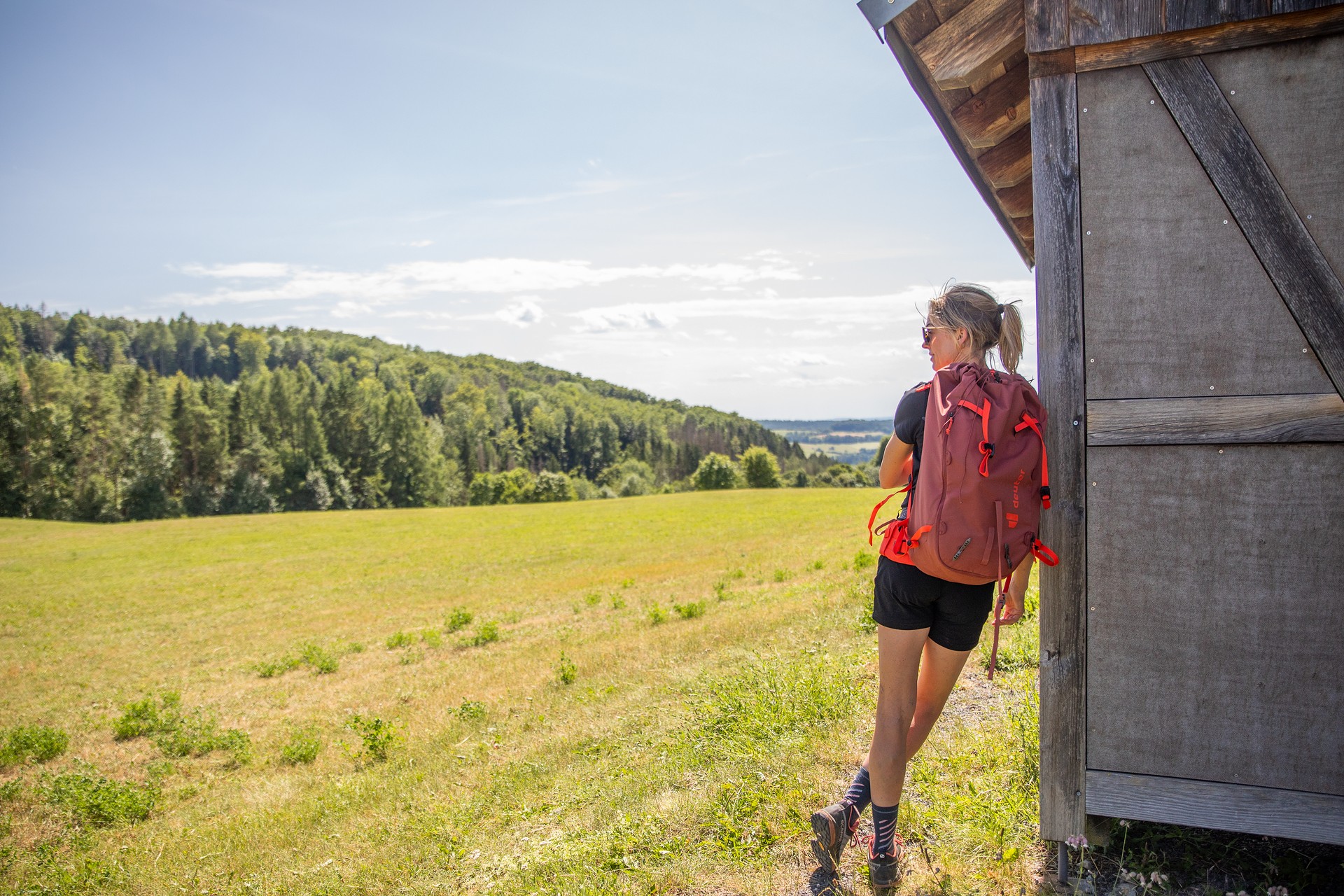 Wanderin auf dem HOCHRHÖNER lehnt an einer Hütte.