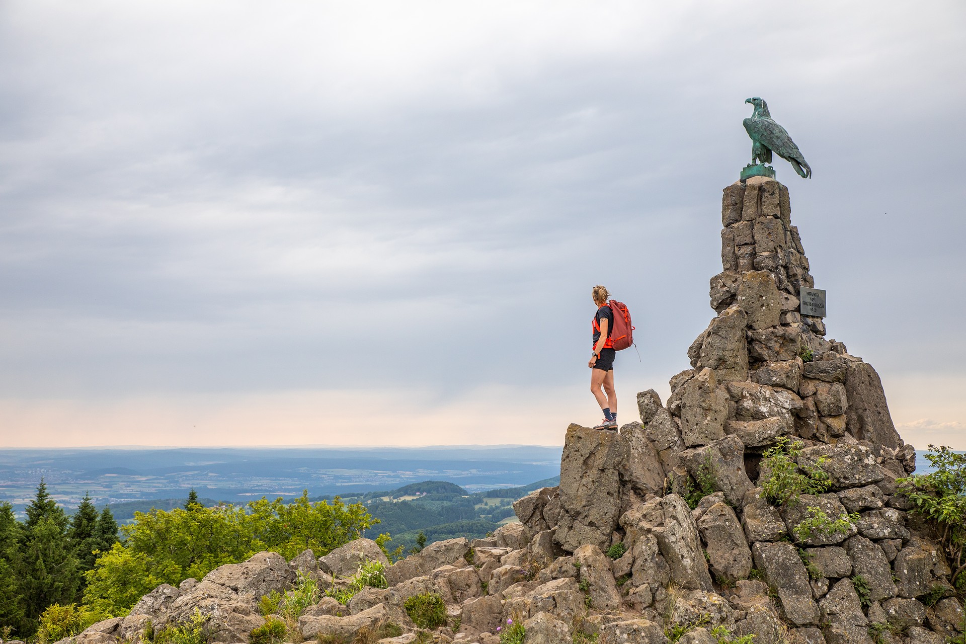 Wanderin steht neben dem Fliegerdenkmal und blickt in die Ferne.