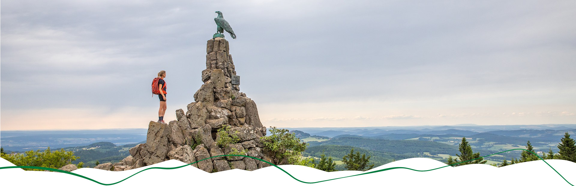 Wanderin steht neben dem Fliegerdenkmal und blickt in die Ferne.