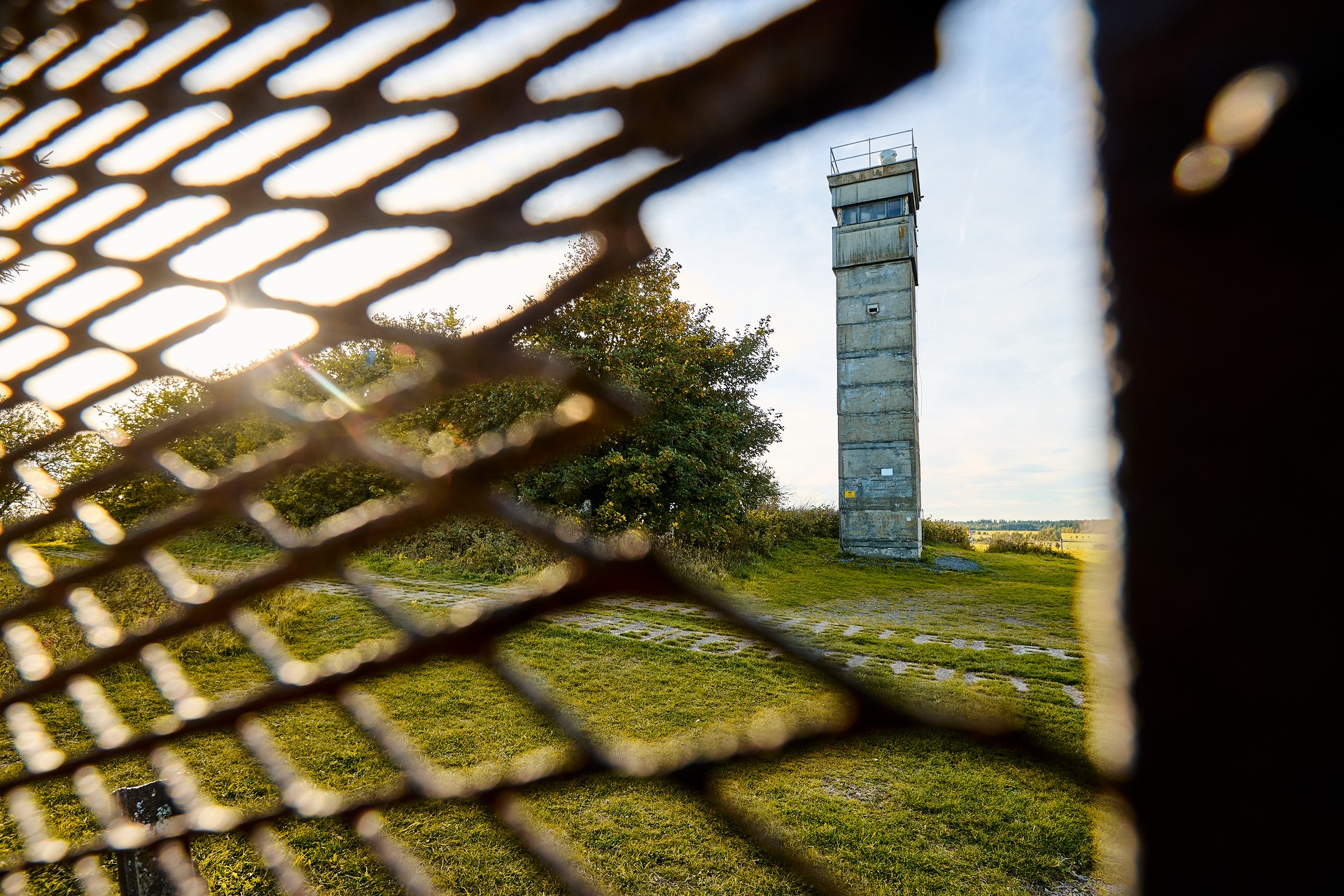 Blick durch einen Metallzaun auf den ehemaligen Grenzturm.