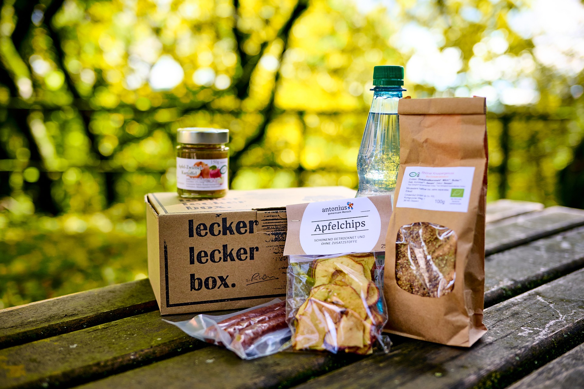 Tragebeutel mit Wasserflasche, Knäckebrot, Flyern, Apfel, Aufstrich und Würstchen.