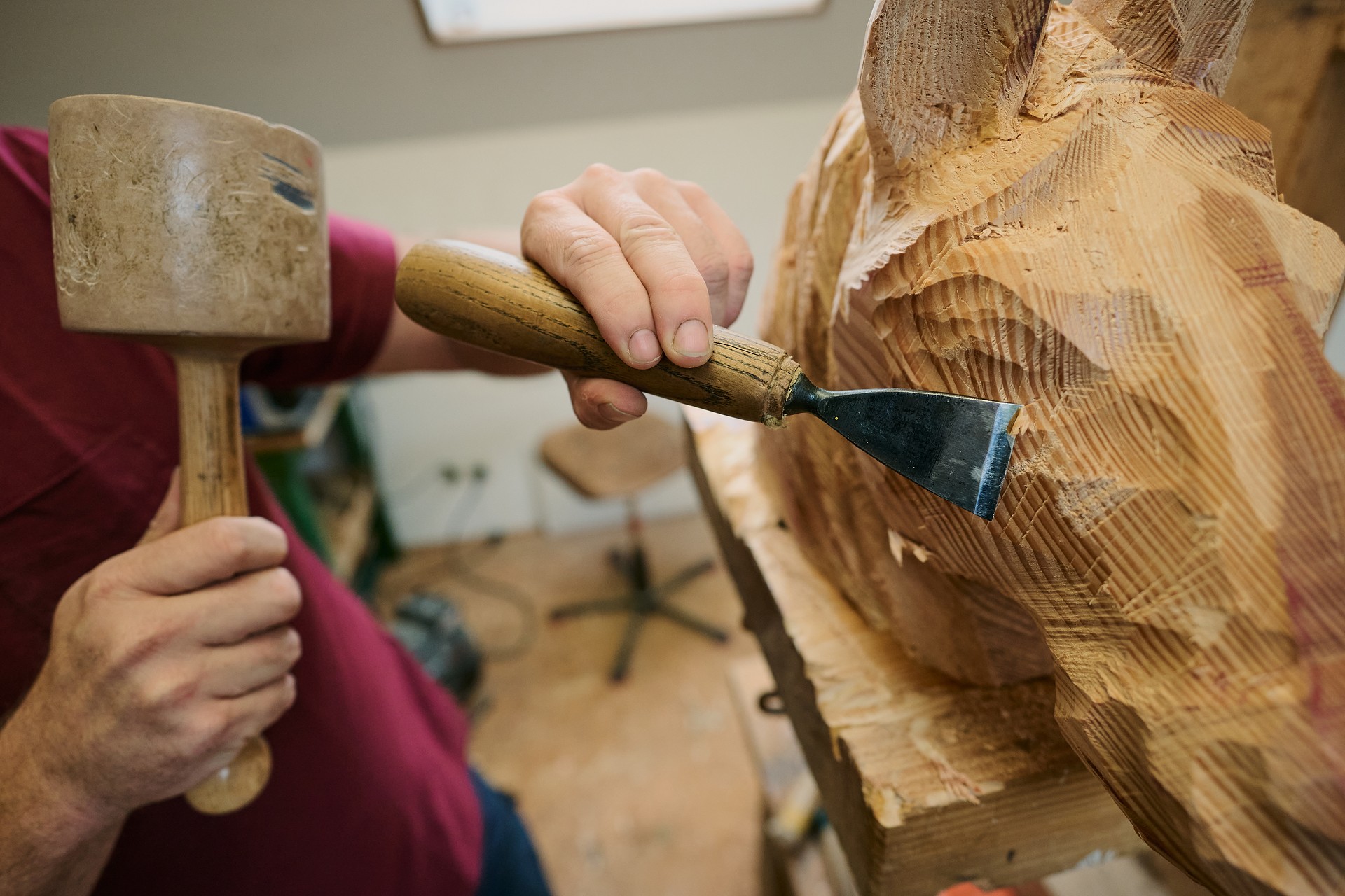 Zwei Hände, die mit Hammer und Meisel das Gesicht eines Pferdes aus Holz schnitzen.