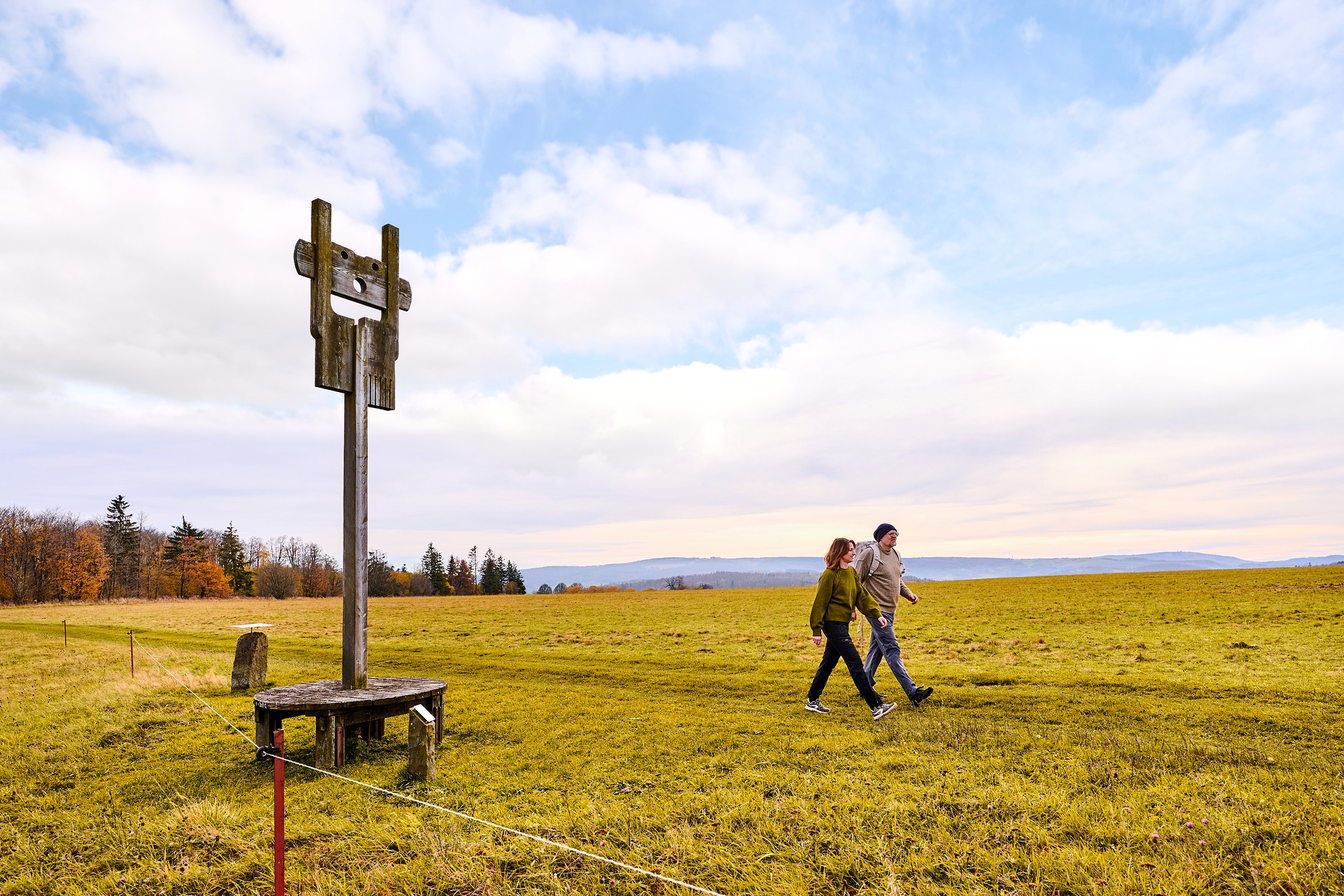 Zwei Personen wandern entlang einer Kunstfigur aus Holz.