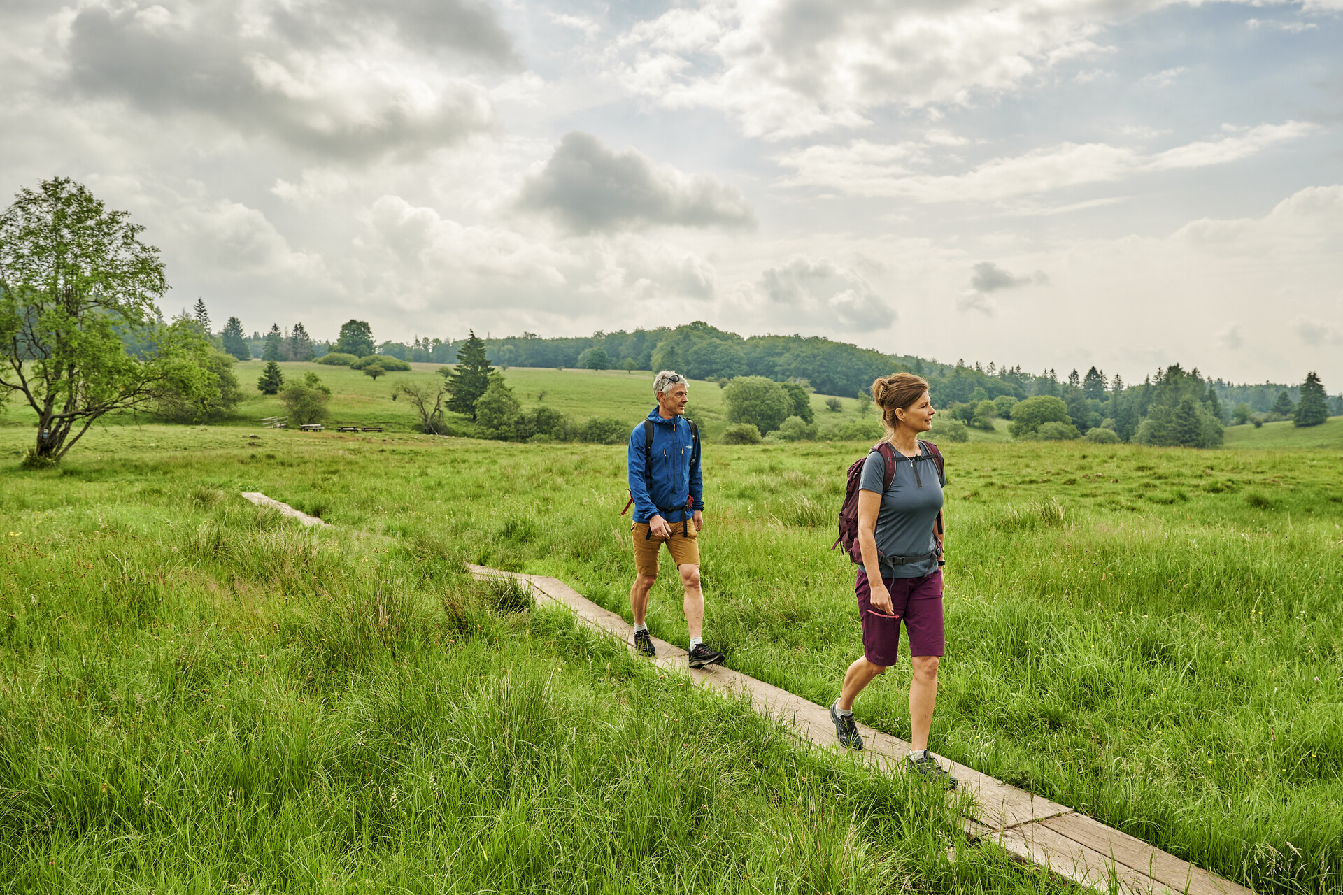 Wanderndes Pärchen auf Holzsteg in grüner Landschaft.